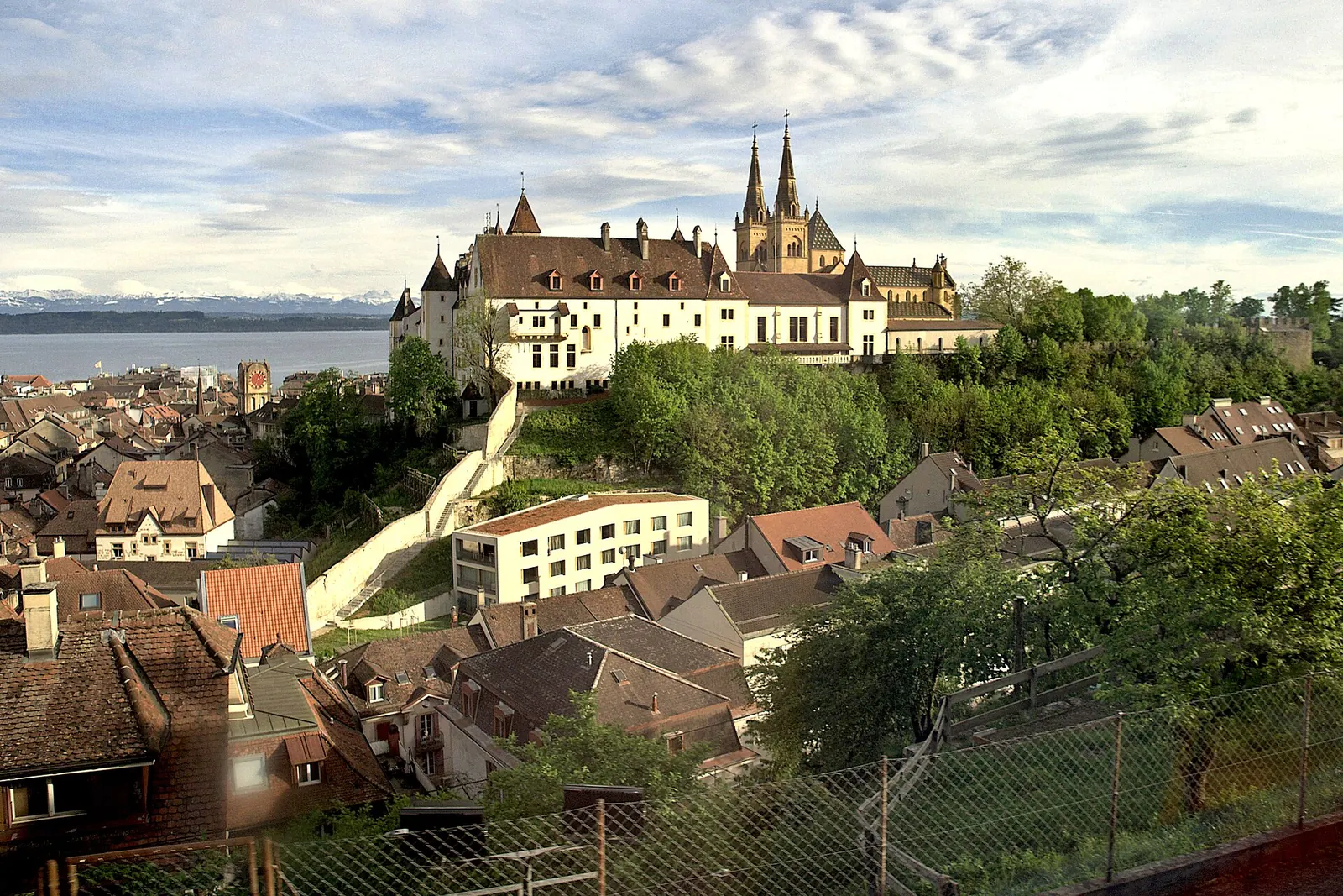 Deux personnes assises au bord du lac de Neuchâtel au coucher du soleil, avec les Alpes à l'horizon