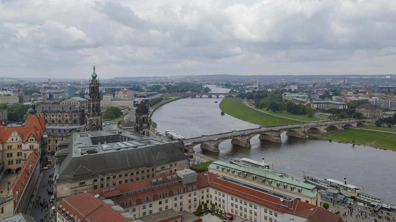 Paar sitzt bei Sonnenuntergang auf den Elbwiesen in Dresden, gegenüber die Silhouette der Altstadt mit der Frauenkirche