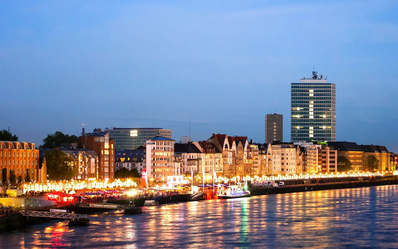 Paar sitzt am Abend auf den Stufen der Rheinuferpromenade in Düsseldorf, im Hintergrund der Rheinturm