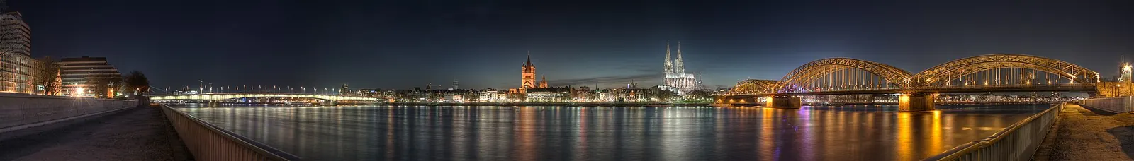 Paar spaziert bei Abendlicht über die Hohenzollernbrücke in Köln, im Hintergrund der Dom