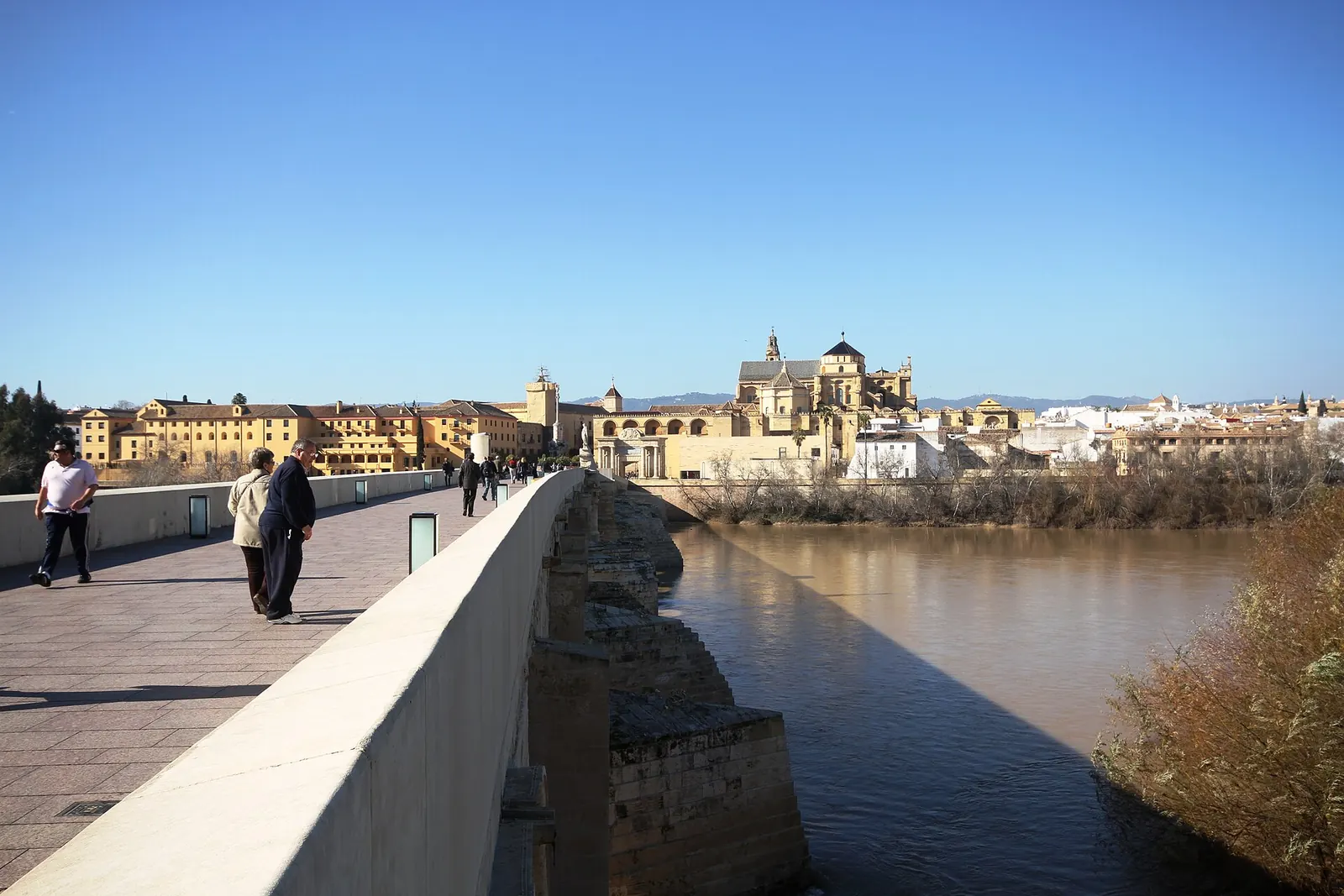 Pareja cruzando el Puente Romano de Córdoba al atardecer con la Mezquita-Catedral al fondo