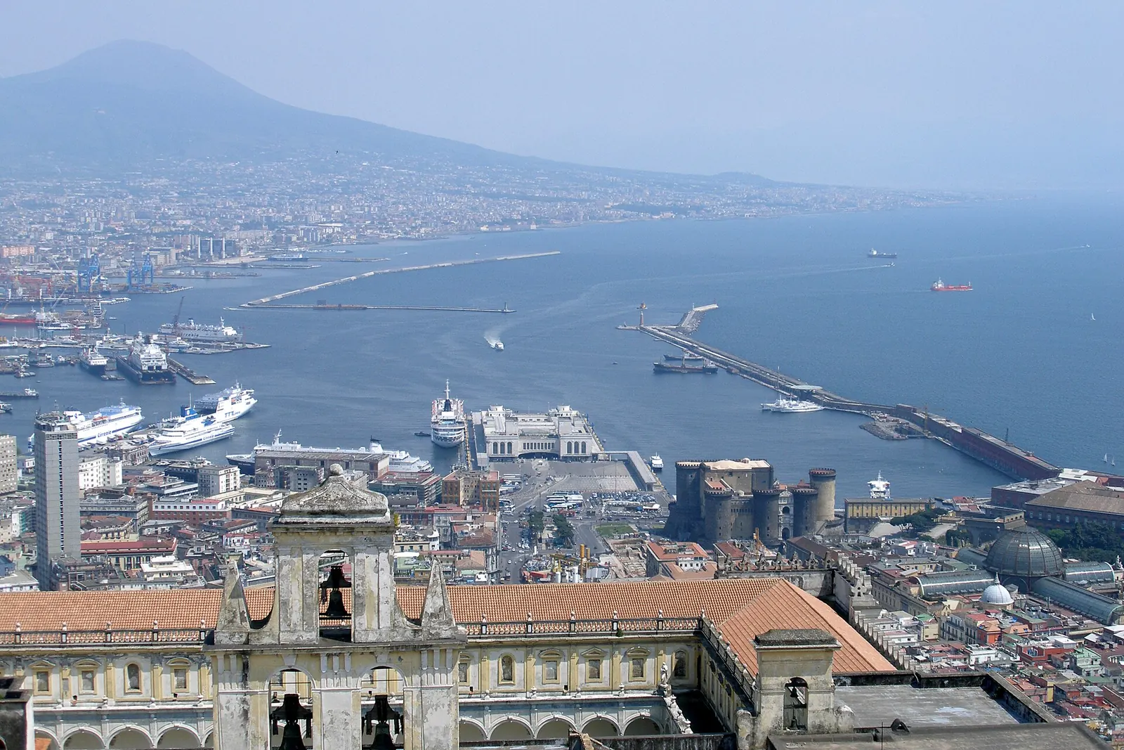 Una coppia sorridente cammina sul lungomare di Napoli, con Castel dell'Ovo e il Vesuvio sullo sfondo
