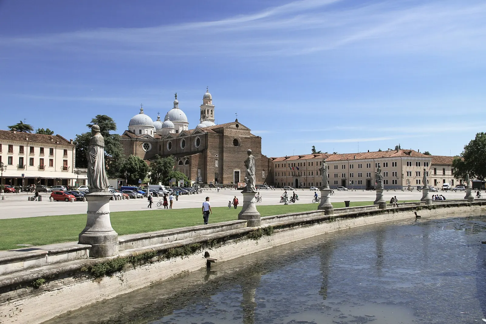 Una coppia passeggia lungo il canale che circonda l'isola Memmia in Prato della Valle a Padova, tra le statue, in una sera d'estate