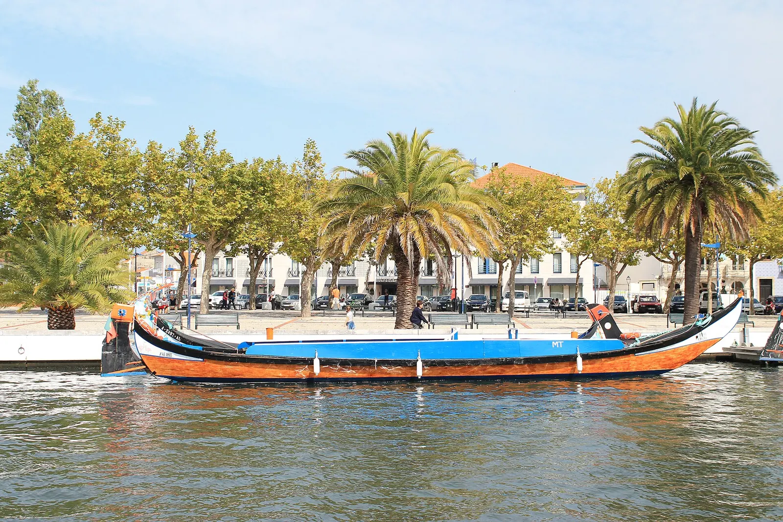 Casal a passear junto ao Canal Central de Aveiro, com moliceiros coloridos na água