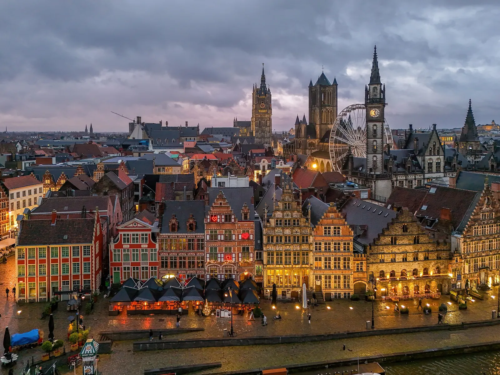 Deux personnes qui trinquent en terrasse sur une place pavée d'une ville belge, en fin de journée