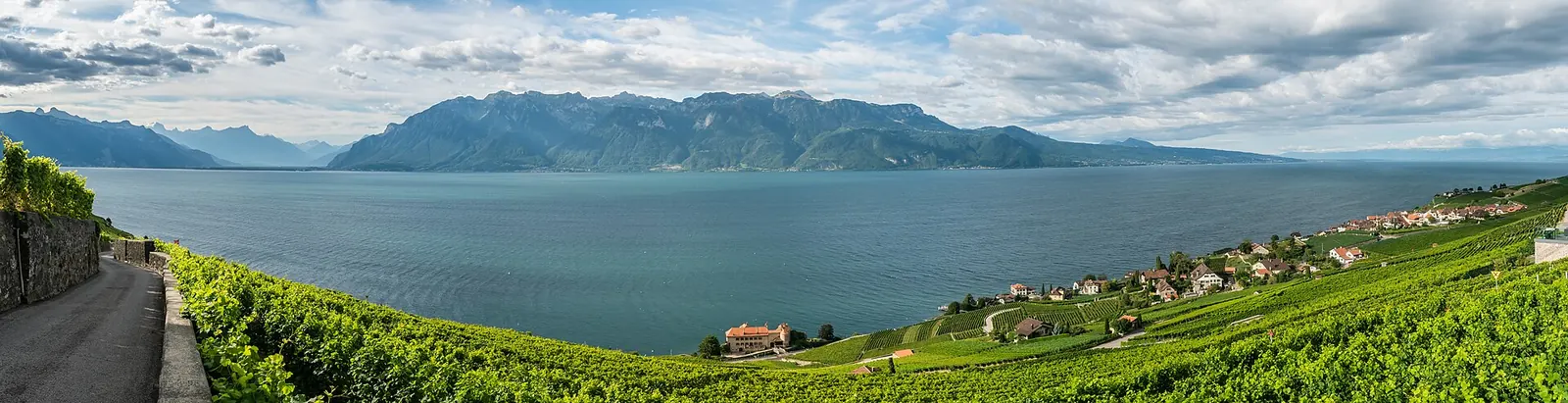 Deux personnes qui se promènent sur un quai au bord du Léman, avec les Alpes au loin